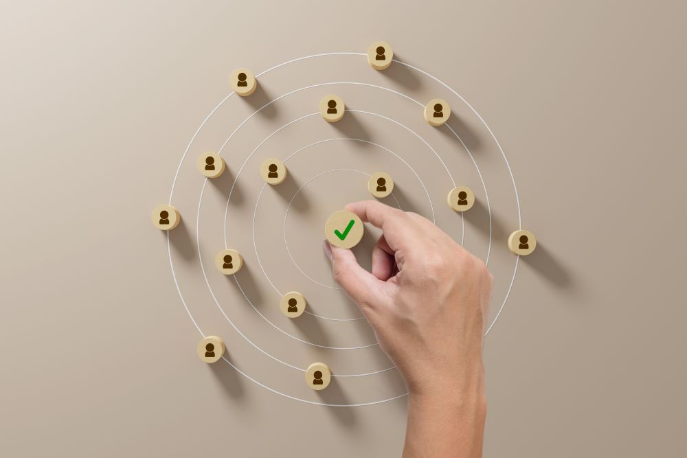 hand holding a wooden piece with a checkmark while other pieces with images of people surround them